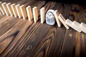 Project risk management represented as chain reaction, businessman letting or preventing dominoes continuous toppling on rustic wooden desk.